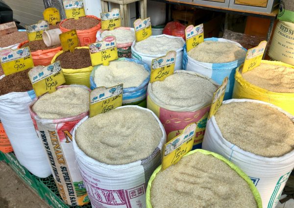 Different types of grains in bags with price tags at a bustling local market.